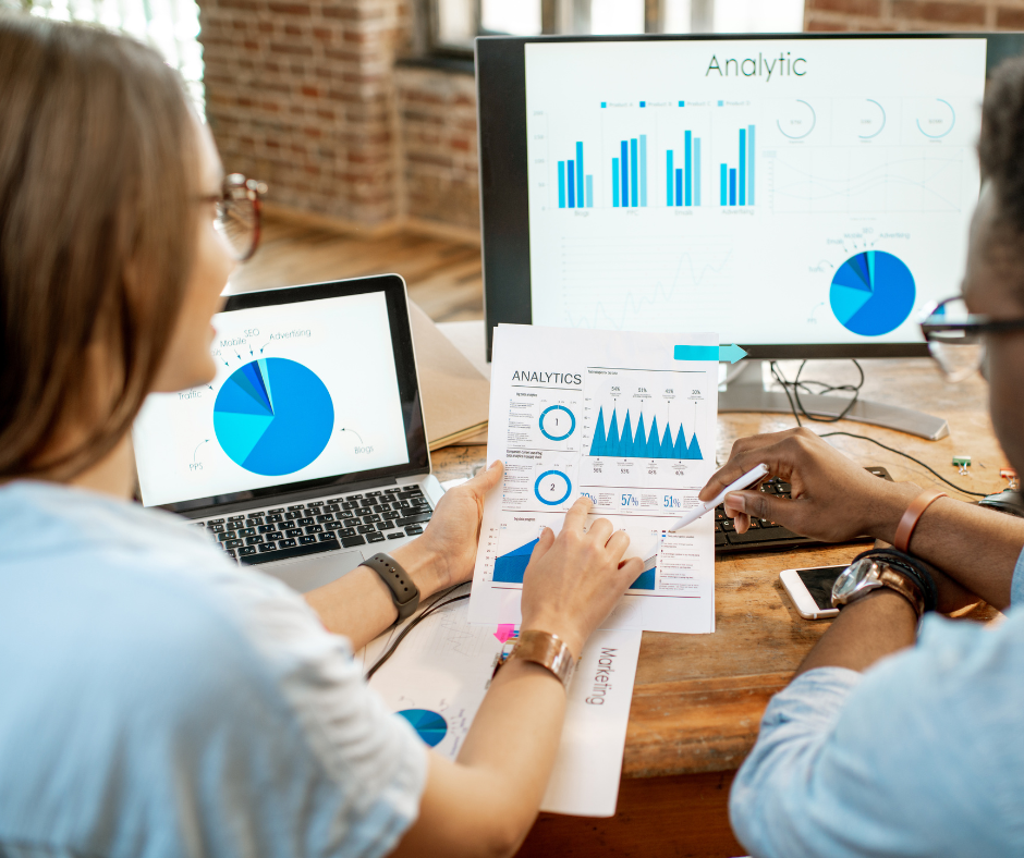 imagem mostra duas pessoas em frente ao computador e tablet analisando dados